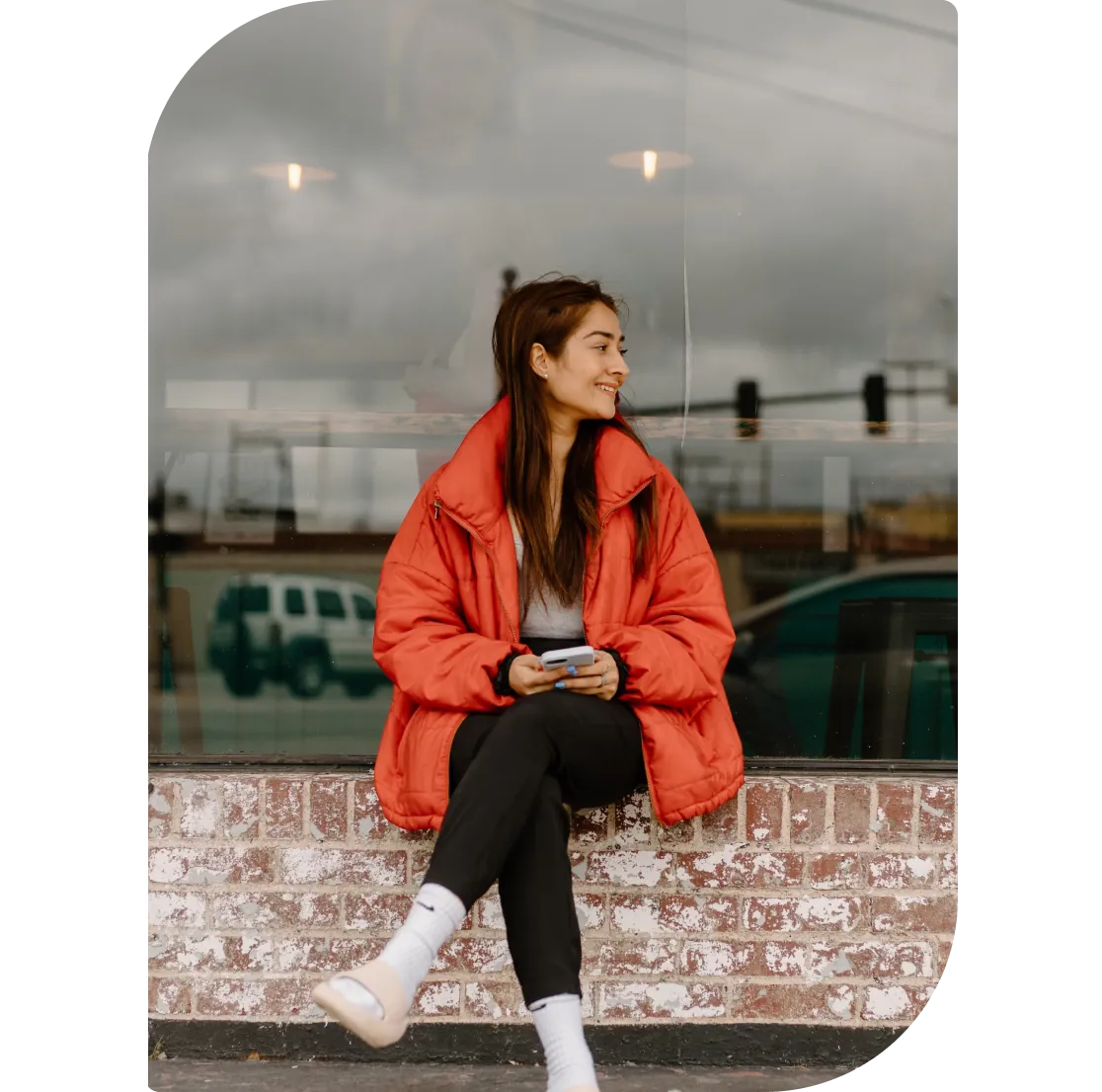 A student sitting on a window ledge with her phone, smiling
